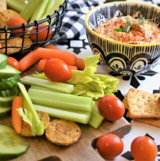 chipotle almond dip in black and white dip bowl with veggies and crackers in black wire basket and on cutting board