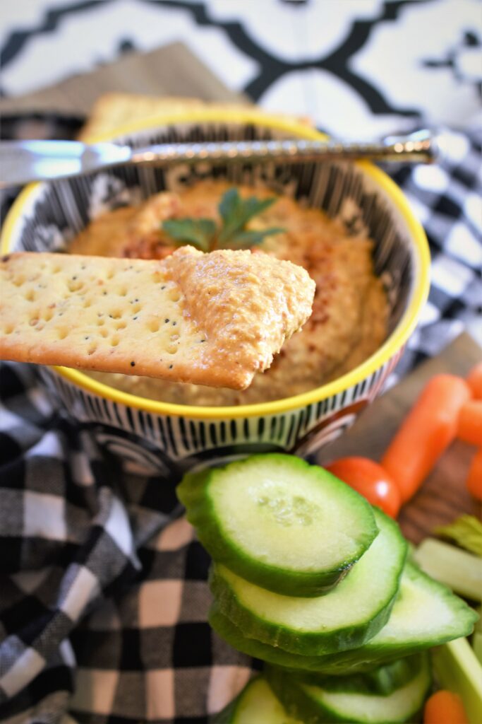 up close image of dip on cracker over dip bowl with veggies off to the side