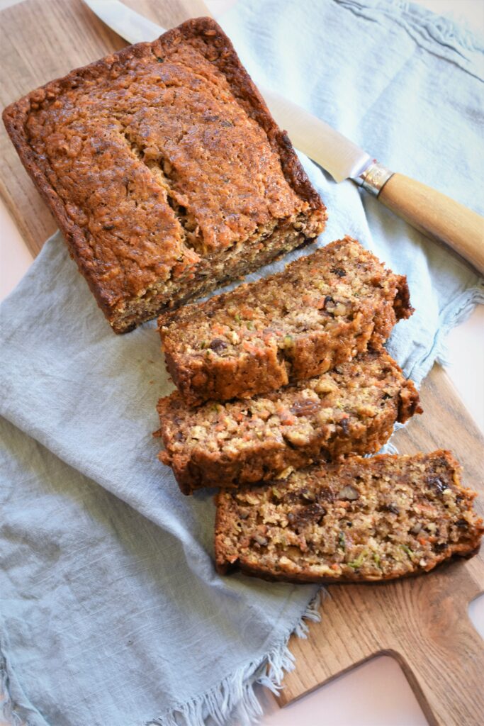 above image of Banana Zucchini Carrot Bread with some sliced on top of fringed light blue towel on top of handled cutting board along size antique bone handled knife 