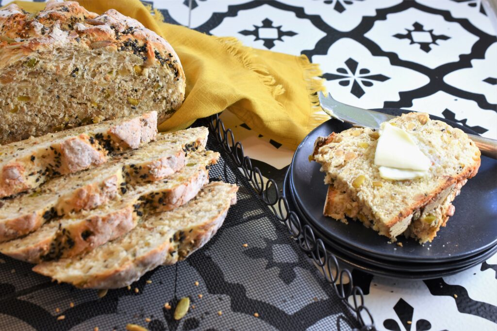 homemade sliced nut and seed bread on cooling rack with slices on a stack of black plates with pats of butter