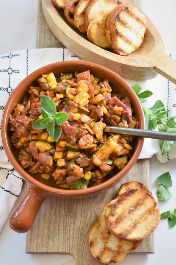 Sicilian zucchini corn gusto in terracotta bowl with small wood bowl of grilled baguette toasts 