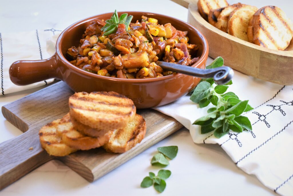 vegetable capanata in ceramic bowl on wood cutting board with grilled toasts 