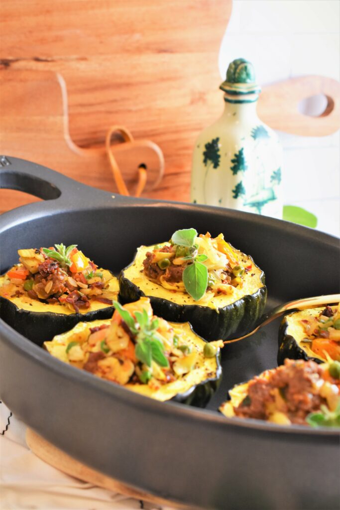 oval black serving dish with Beyond Stuffed Acorn Squash on counter with two cutting boards and an antique ceramic olive oil bottle in the background