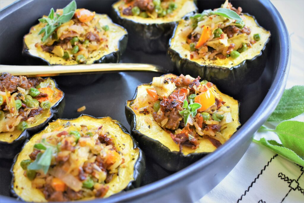 view of several portions of small squash in black casserole with gold serving spoon garnished with fresh sage