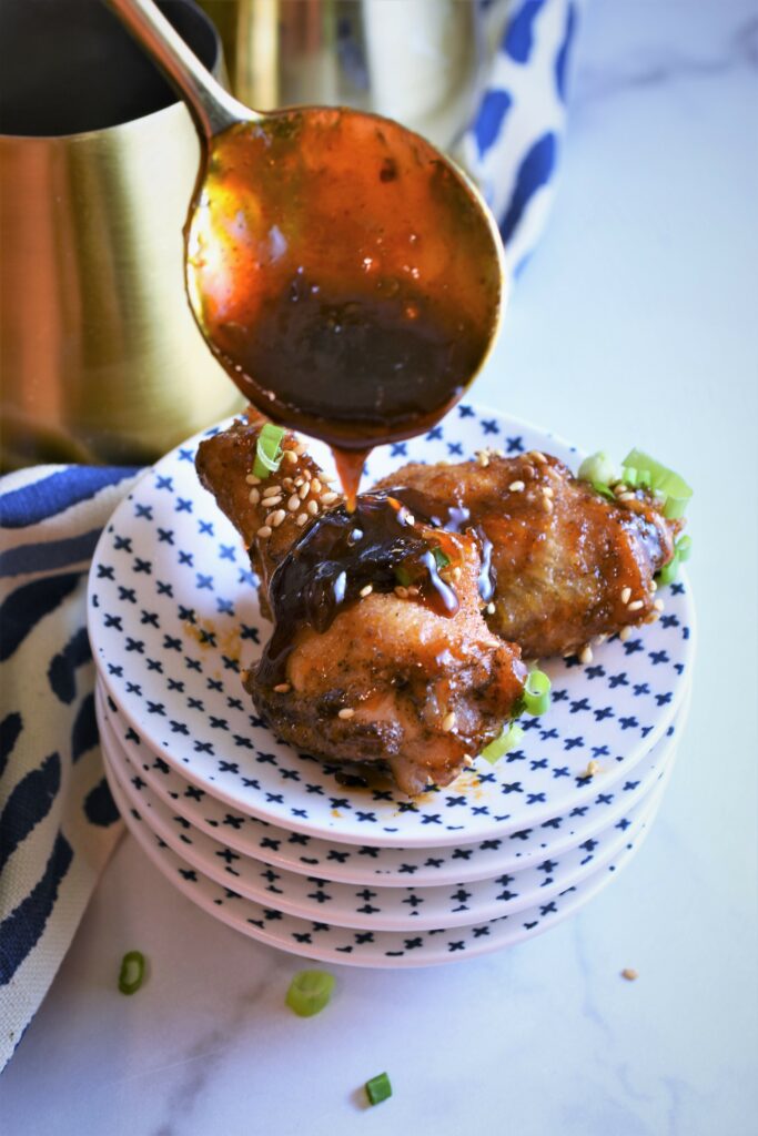 stack of mini plates with mini chicken legs with sauce dripping off brass spoon onto it