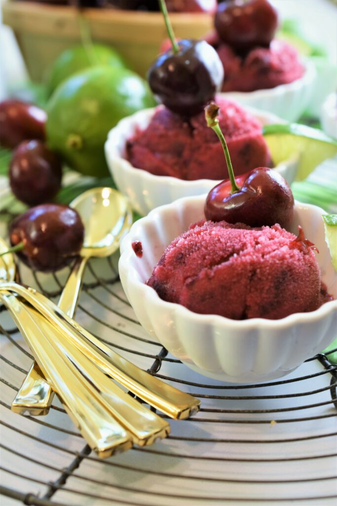 up close image of sorbet garnished with a fresh cherry with a stem among gold dessert spoons