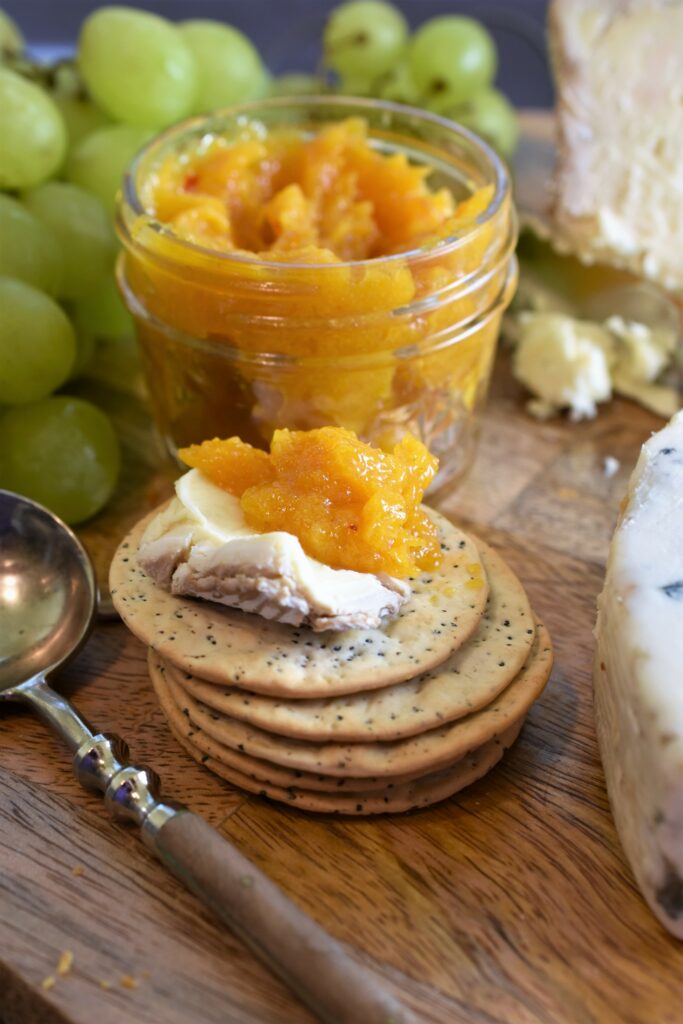 up close jar of apricot butter with Moscato, vanilla & rosemary with a stack of crackers with a piece of brie on top with some apricot butter 