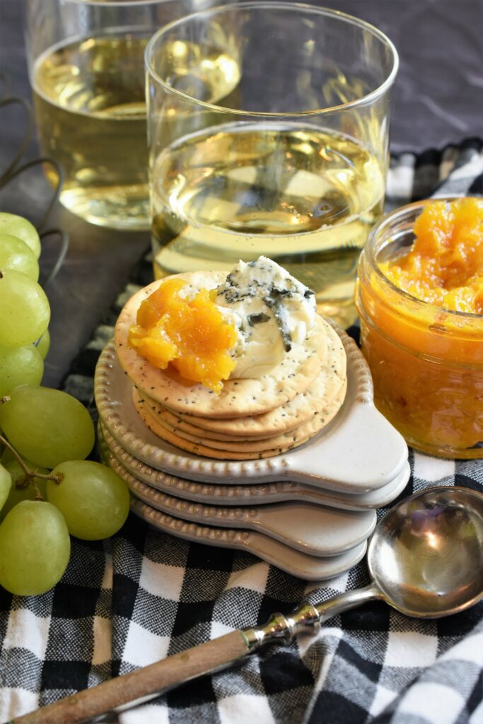 two glasses of white wine with a stack of tiny appetizer plates with a stack of crackers with blue cheese and apricot butter with Moscato, vanilla & rosemary 