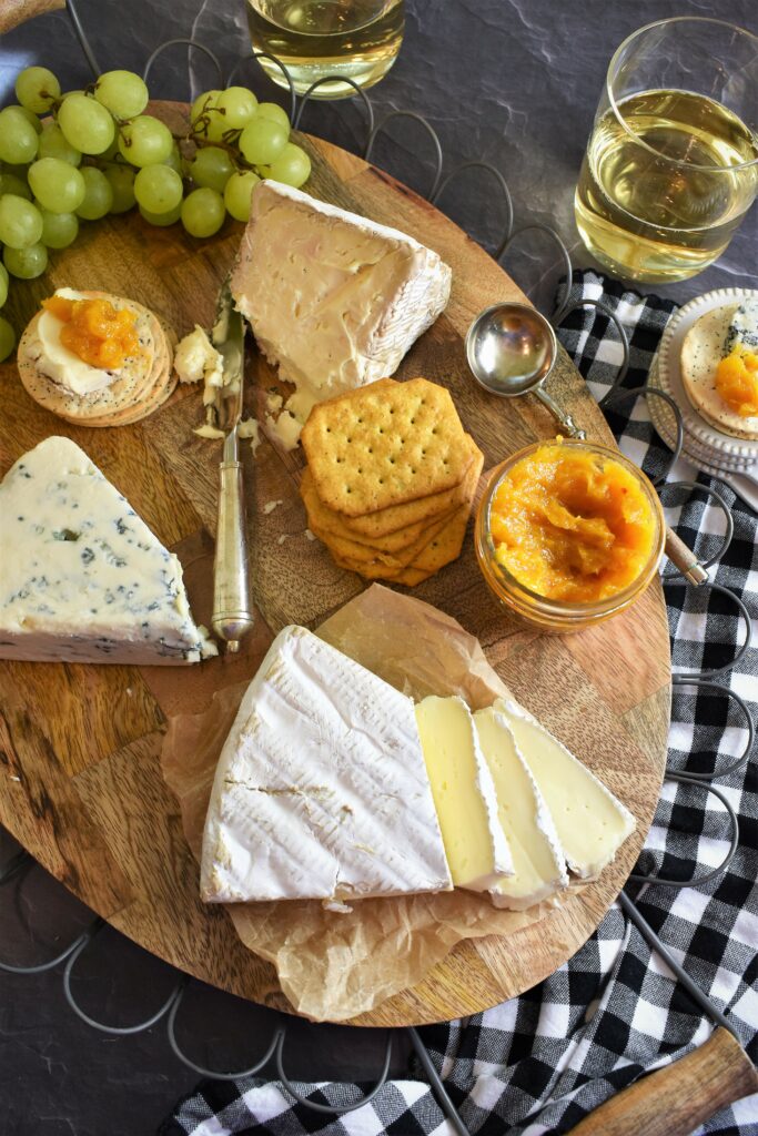 oval wood cutting board edged with scalloped wires with assorted cheese with an open jar of apricot butter with Moscato Vanilla & Rosemary