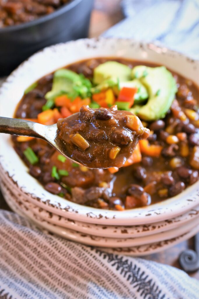 up close view of a black iron soup spoon full of vegan black bean chili with coffee & cocoa