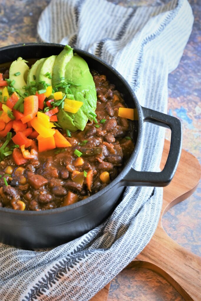 large cooking vessel of vegan chili on cutting board with kitchen towel