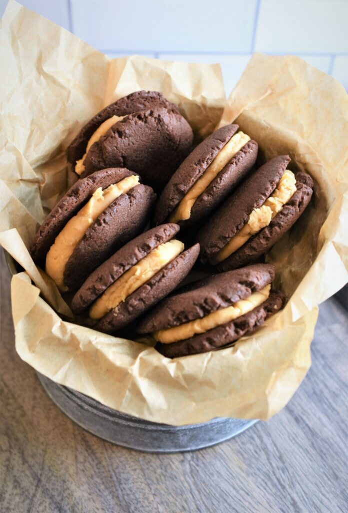 Vegan Chocolate Peanut Butter Sandwich Cookies in galvanized metal cookie tin with tan parchment paper on wood cutting board
