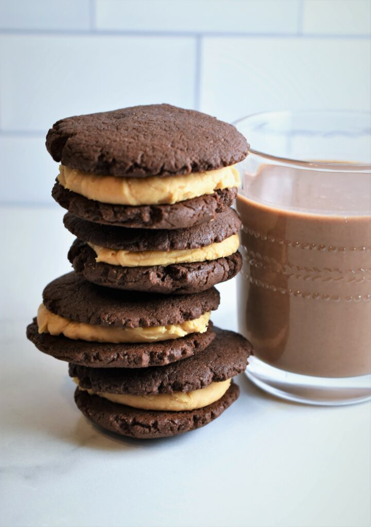 a stack of four vegan sandwich cookies leaning next to a glass of milk