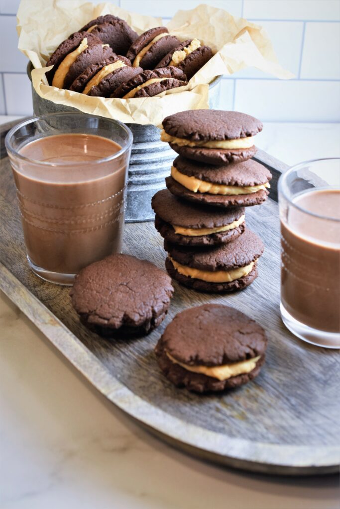 wood platter with two glasses of chocolate milk with a tin of cookies 