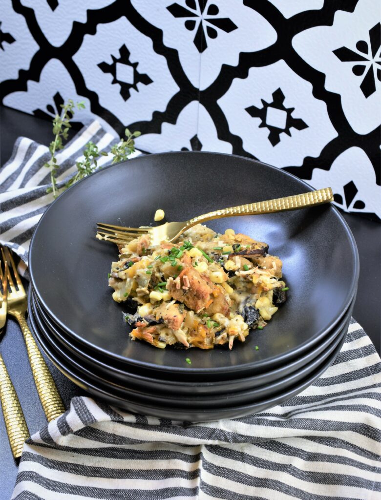 4 stacked black bowls with top bowl with a serving of the casserole with gold fork