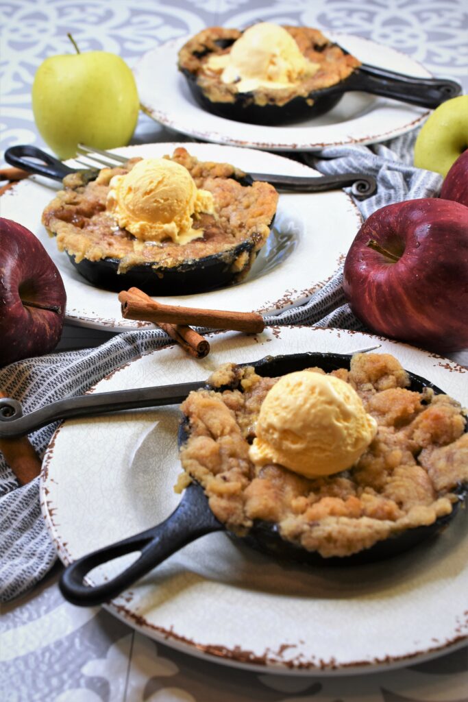 set of 3 small baked country desserts set on top of white rustic plates with whole apples surrounding them