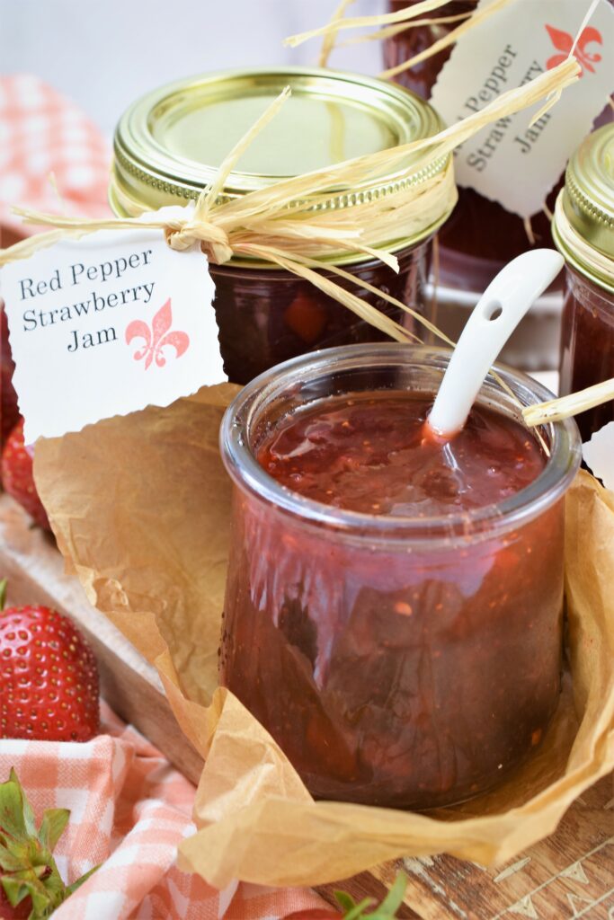 red pepper strawberry jam in mini glass pot with white porcelain spoon on cutting board