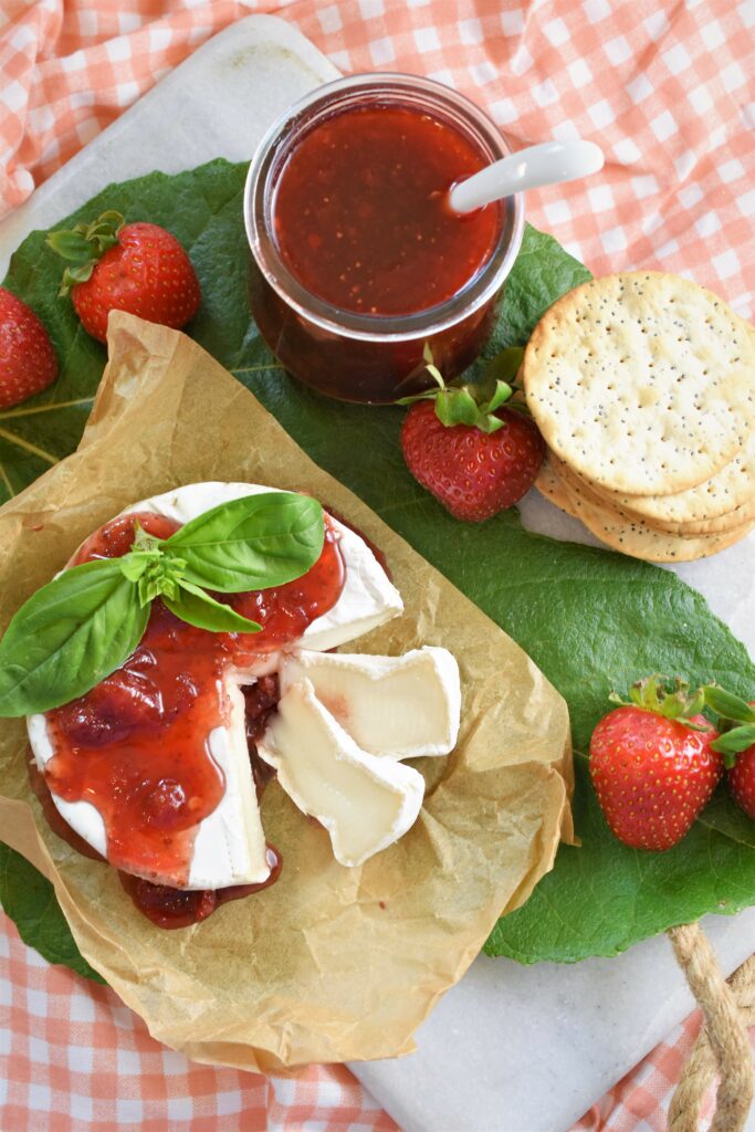 a wheel of goat Brie with jam poured on top garnished with basil on top of a fig leaf
