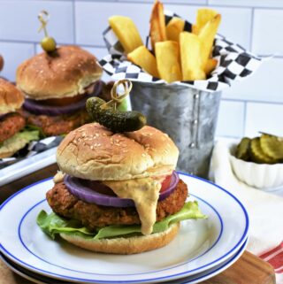 up close image of 1 Chipotle Butternut Squash Burger with others in the background with Hatch Chile Aioli on a blue and white plate with french fries in galvanized steel cup