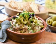 olive sun-dried tomato cream cheese dip in terracotta dish on wood board