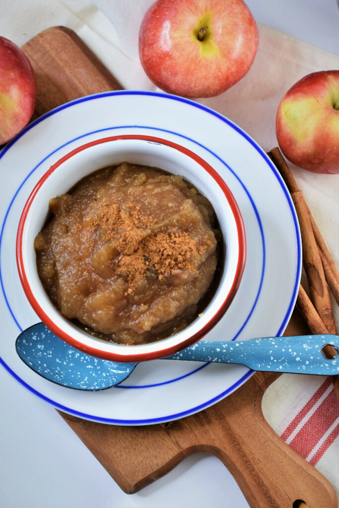 brown sugar spiced applesauce in white and red enameled bowl on blue and white sauce with apples in the background