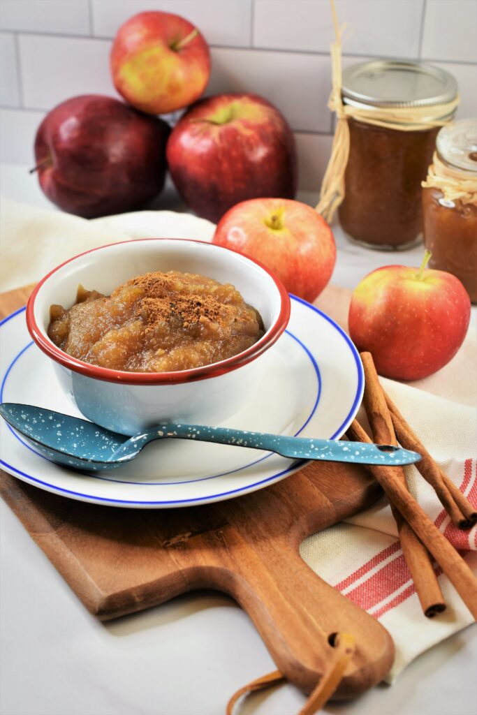 applesauce in white and red enameled bowl on blue and white sauce with apples in the background