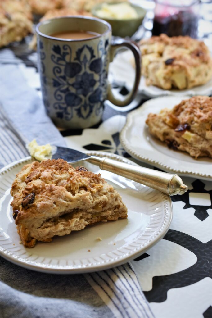 apple cranberry walnut scones on several small ivory plates with a cup of coffee on black and white countertop
