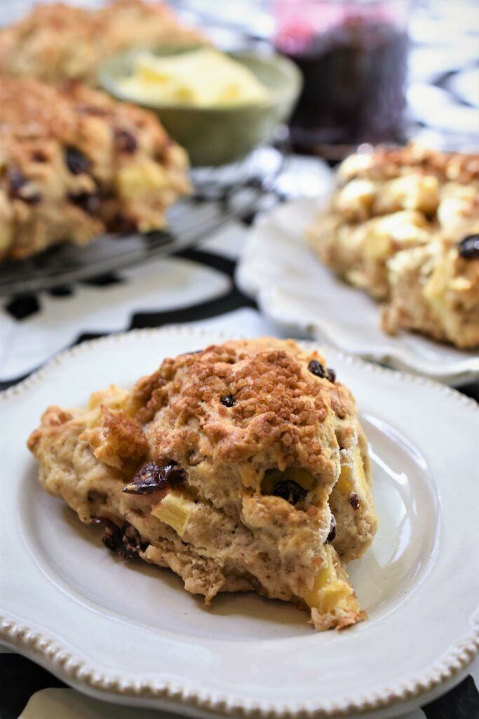 up close image of vegan apple cranberry scone with walnuts on rustic ivory plate