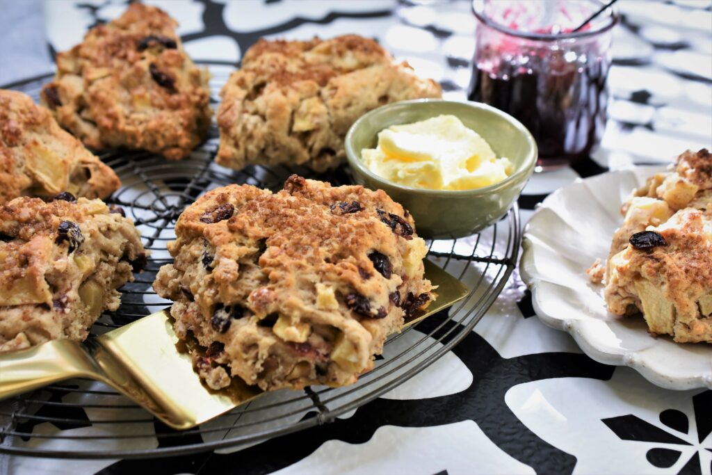 large image of breakfast apple scones on round wire cooling rack with dish of butter and jar of jam