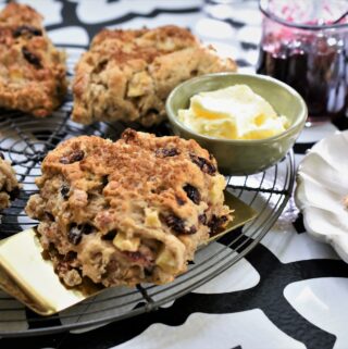 large image of breakfast apple scones on round wire cooling rack with dish of butter and jar of jam