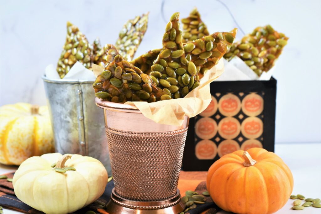 vegan pumpkin seed brittle in mini metal Halloween treat containers with mini pumpkins surrounding