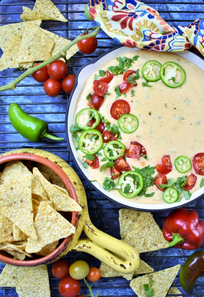 overhead image of Hatch chile queso in frying pan on cooling rack with tortilla chips and fresh tomatoes and peppers