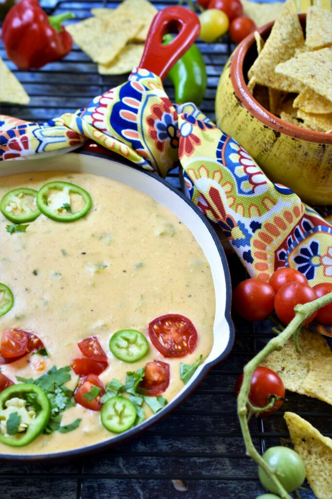 game party dip served in a red cast iron skillet with colorful napkin tied around handle with fresh cherry tomatoes and sliced jalapenos with tortilla chips