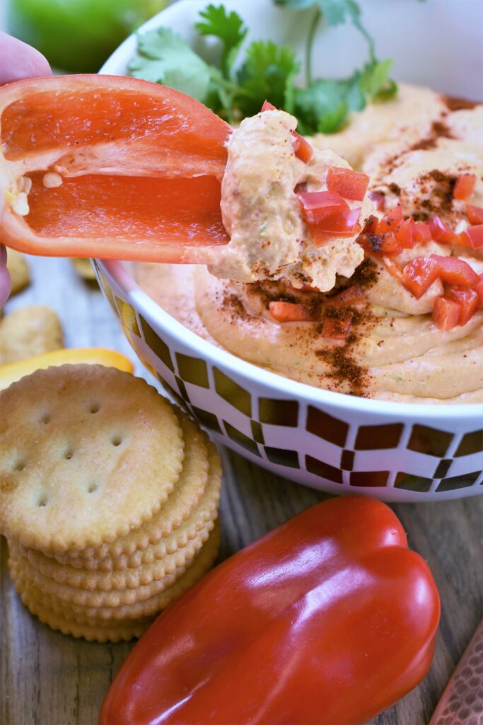 cut mini bell pepper scooping cheese dip out of white and gold dip bowl
