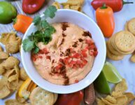 chili pepper cheese dip in white bowl with chips, crackers and veggies for dipping