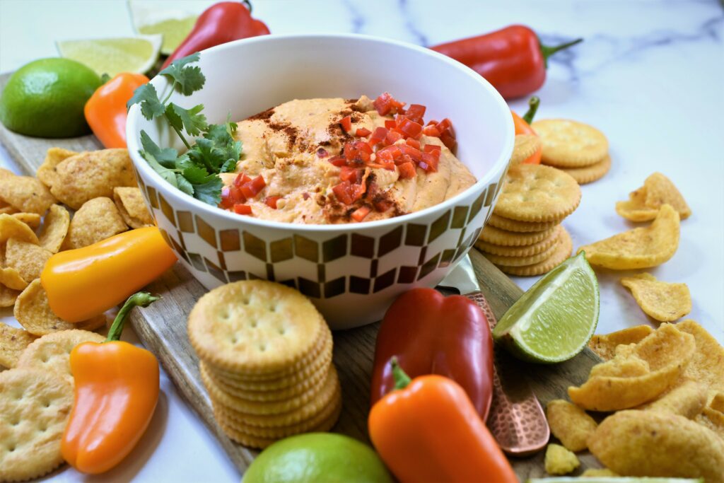 chipotle lime cheddar dip in white and gold modern bowl on cutting board with crackers, corn chips and mini peppers scattered around
