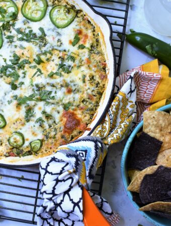 baked Mexican spinach dip in orange cast iron pan on cooling rack with blue and white tortilla chips