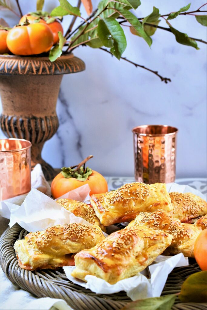 urn with persimmons and twigs with wicker tray of savory appetizers