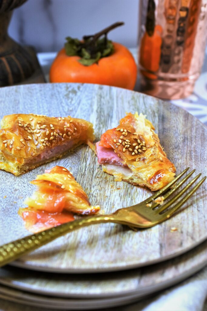 persimmon ham and swiss puffs half eaten on stack of faux wood salad plates with gold fork