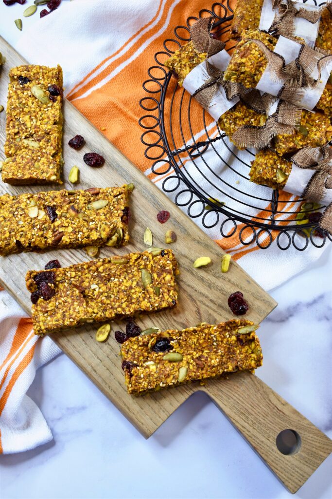round black cooling rack and cutting board filled with pumpkin granola bars on marble countertop with orange and white dish towel