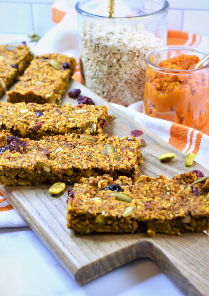 Fall oat bars with nuts and seeds on bread board with jar of oatmeal and jar of pumpkin puree