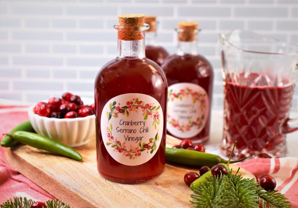 infused chili cranberry vinegar in corked bottle on cutting board with fresh cranberries in small with scalloped bowl