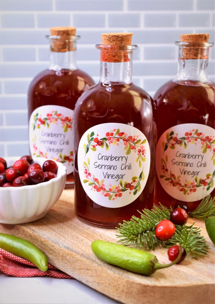 cranberry serrano chili vinegar in corked bottles on cutting board with a small bowl of fresh cranberries