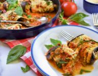 vegan stuffed eggplant rollatini on white and blue plate with blue cast iron skillet in background